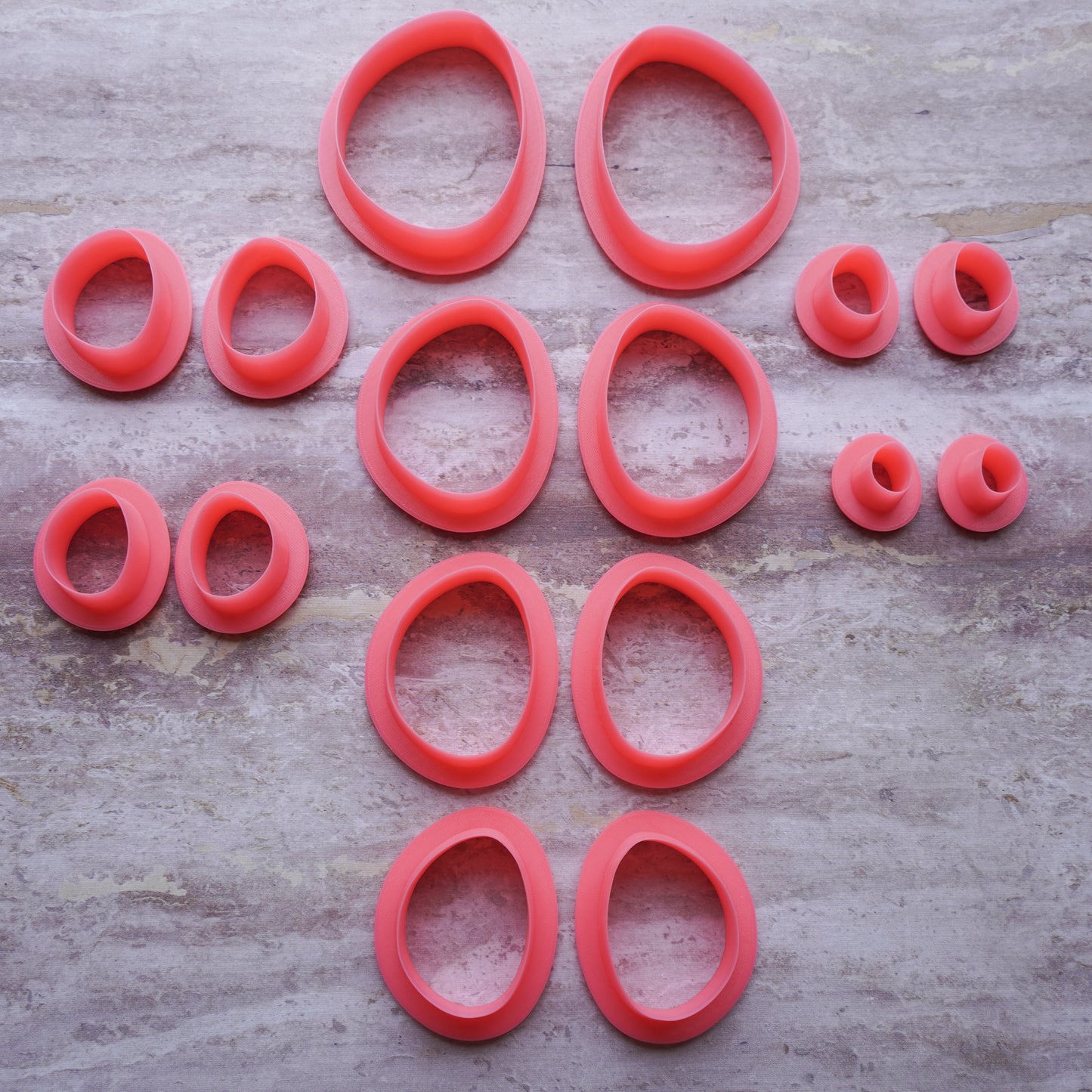 All available sizes of the pink polymer clay cutters in the Sabi drop shape. These cutters are sitting on top of a mauve-marbled stone background.