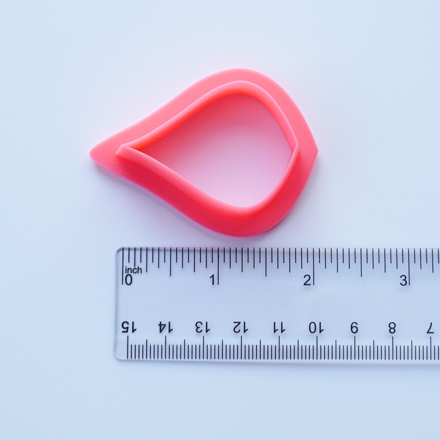 Pink pear shaped clay cutter is shown above a ruler that measures 1.75 inch.