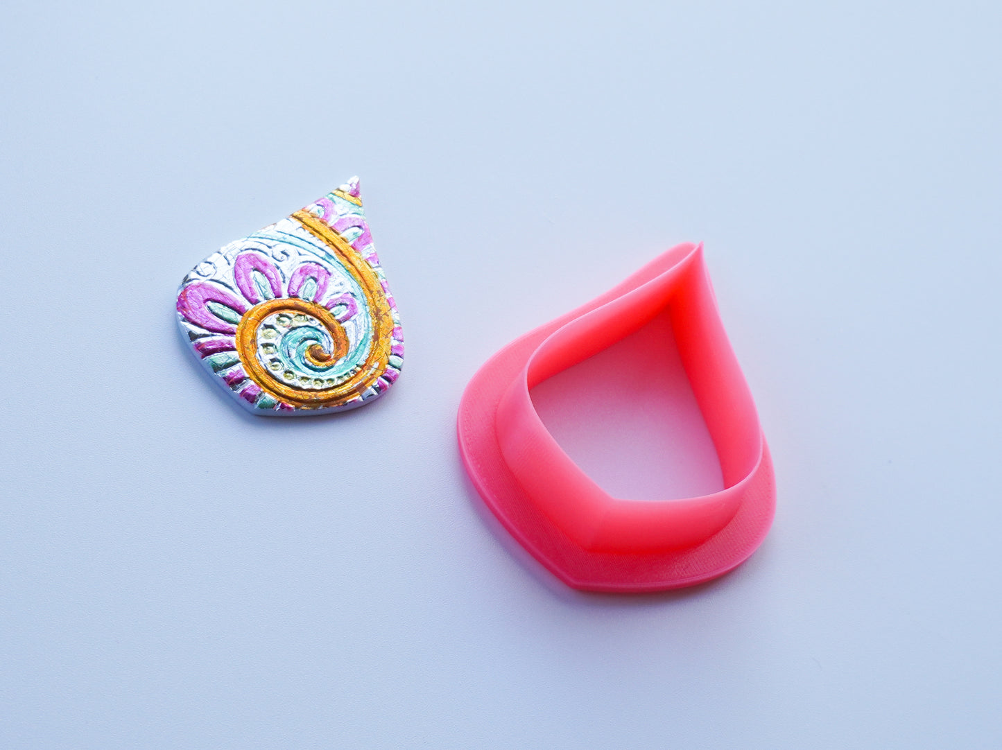 Pink pear shaped clay cutter adjacent to piece of polymer clay art created with the pear shaped clay cutter.