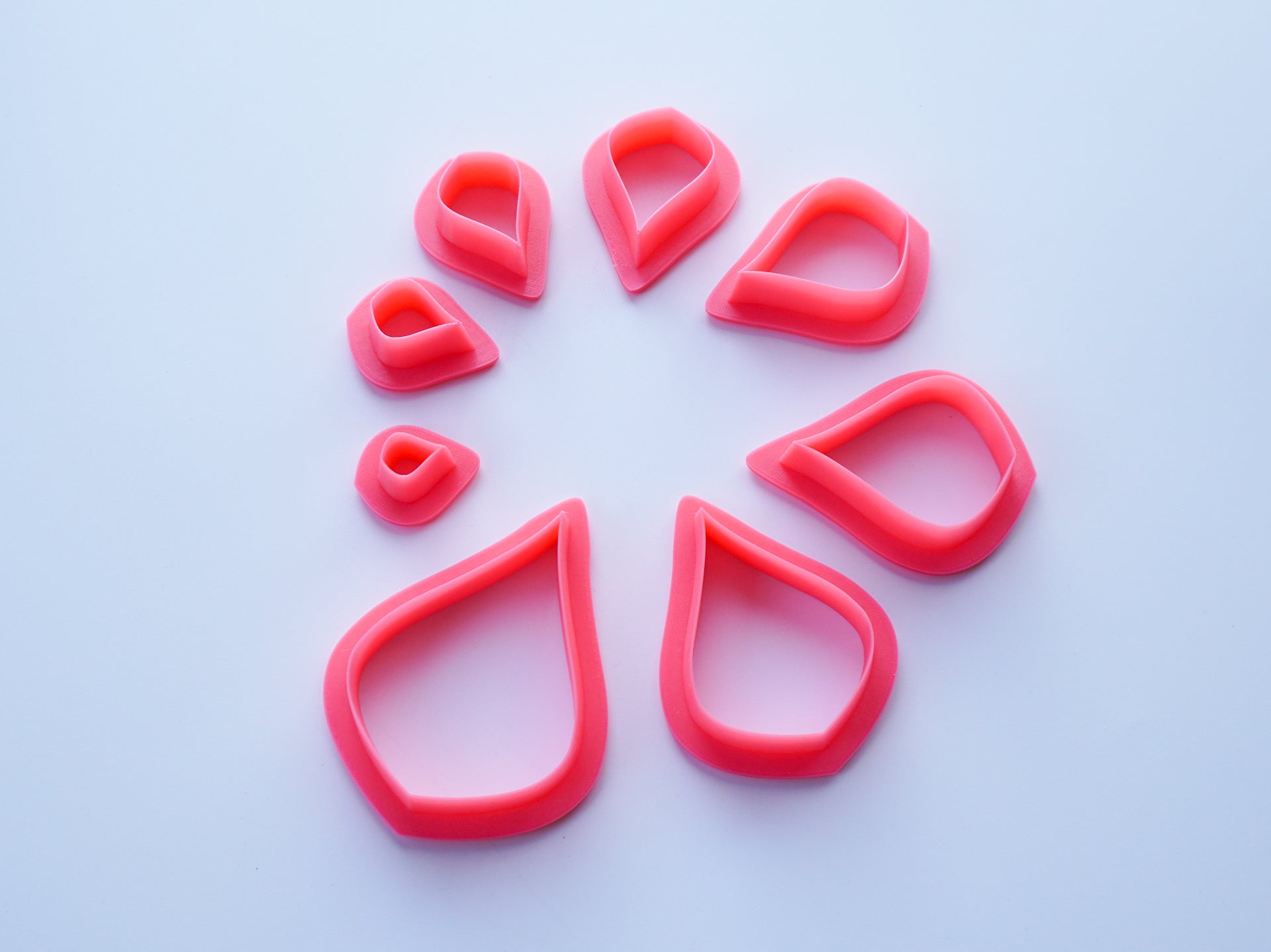 Pink pear shaped polymer clay cutters shown in a circular pattern of all available sizes.