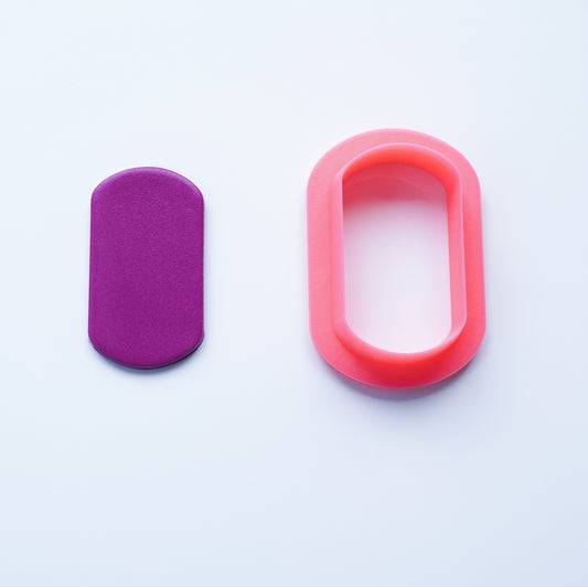 Dog tag-shaped polymer clay cutter 3D printed in pink PLA filament alongside cutout of berry-colored polymer clay.