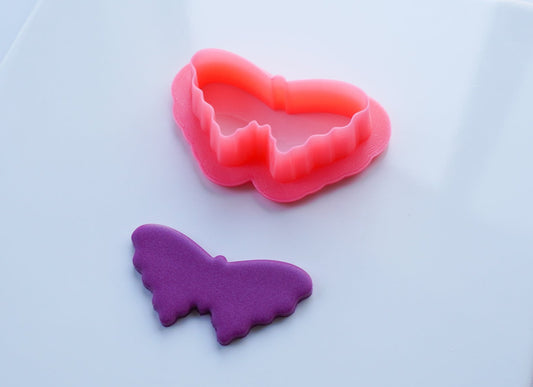 Pink butterfly clay cutter with sample cut out of purple clay on a white ceramic tile